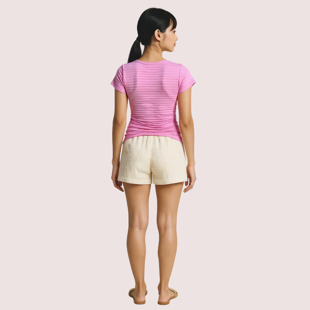Woman wearing a pink striped shirt and beige shorts on a light pink background